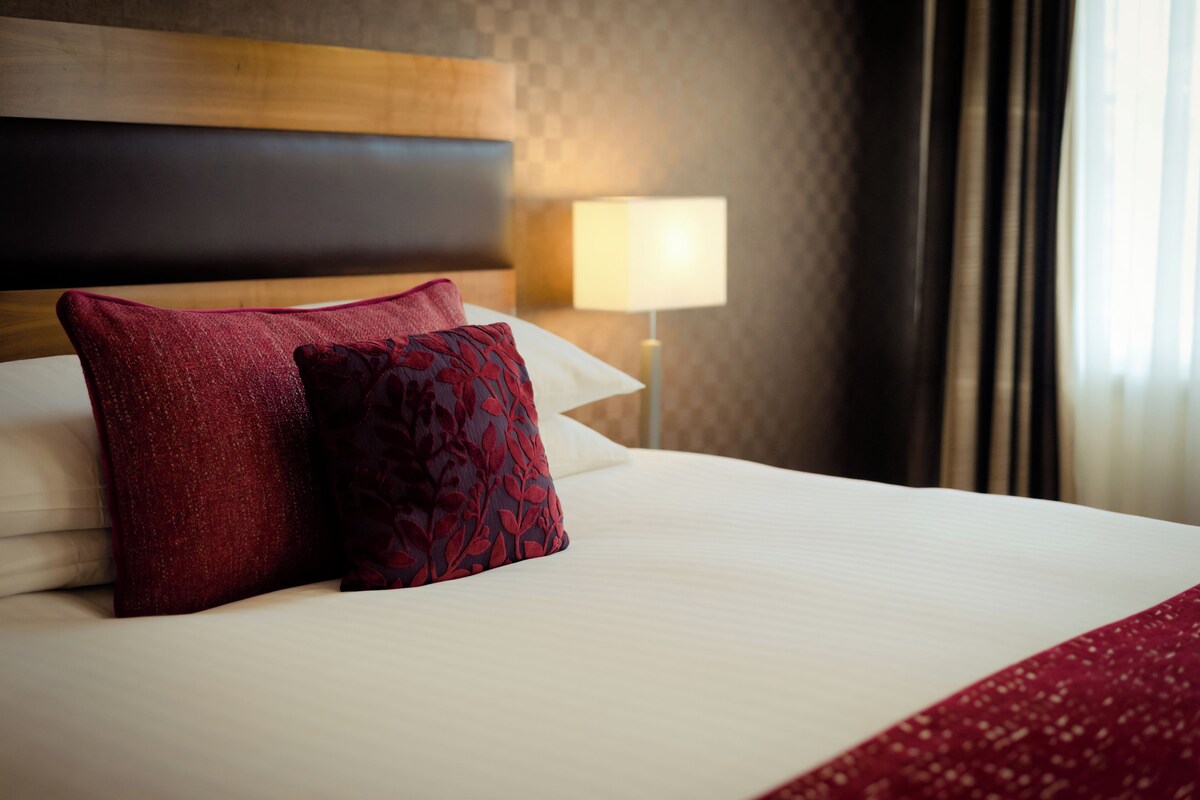 A neatly made bed with a white comforter and two red pillows.