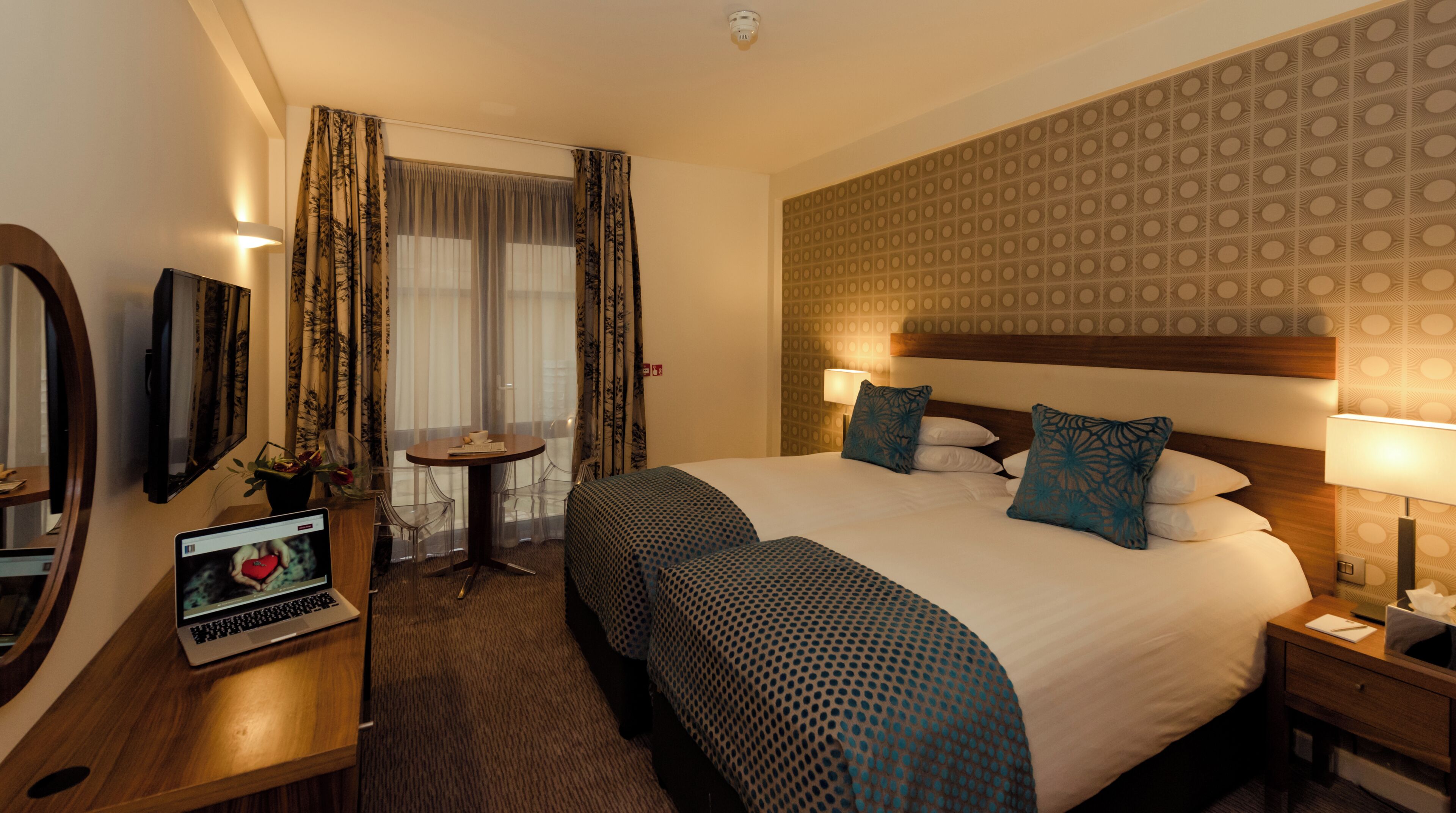Een hotelkamer met een groot bed, een bureau met een laptop, een televisie en een raam met gordijnen.