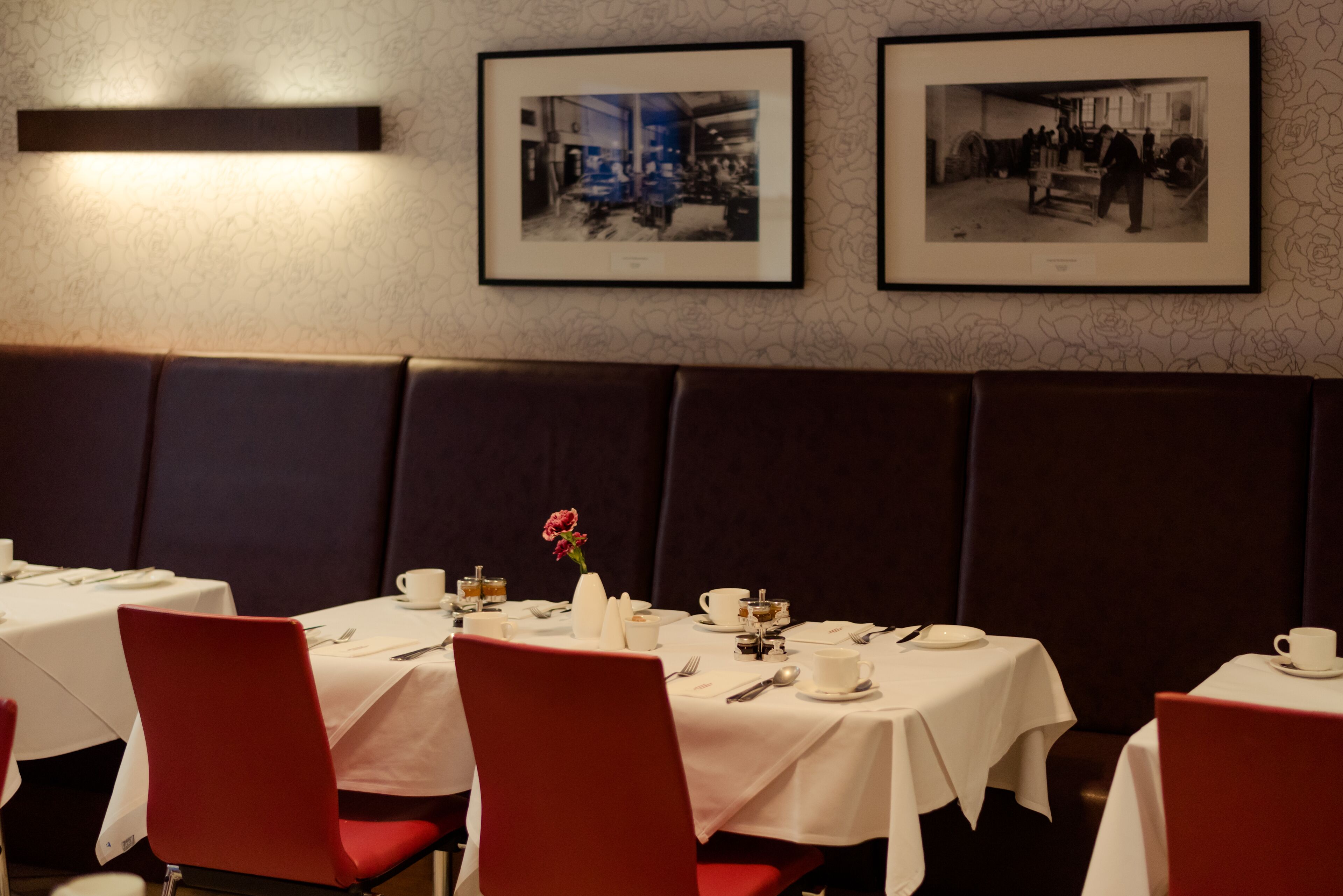 A dining area with tables set for service, framed pictures on the wall, and a dark-colored booth seating area.