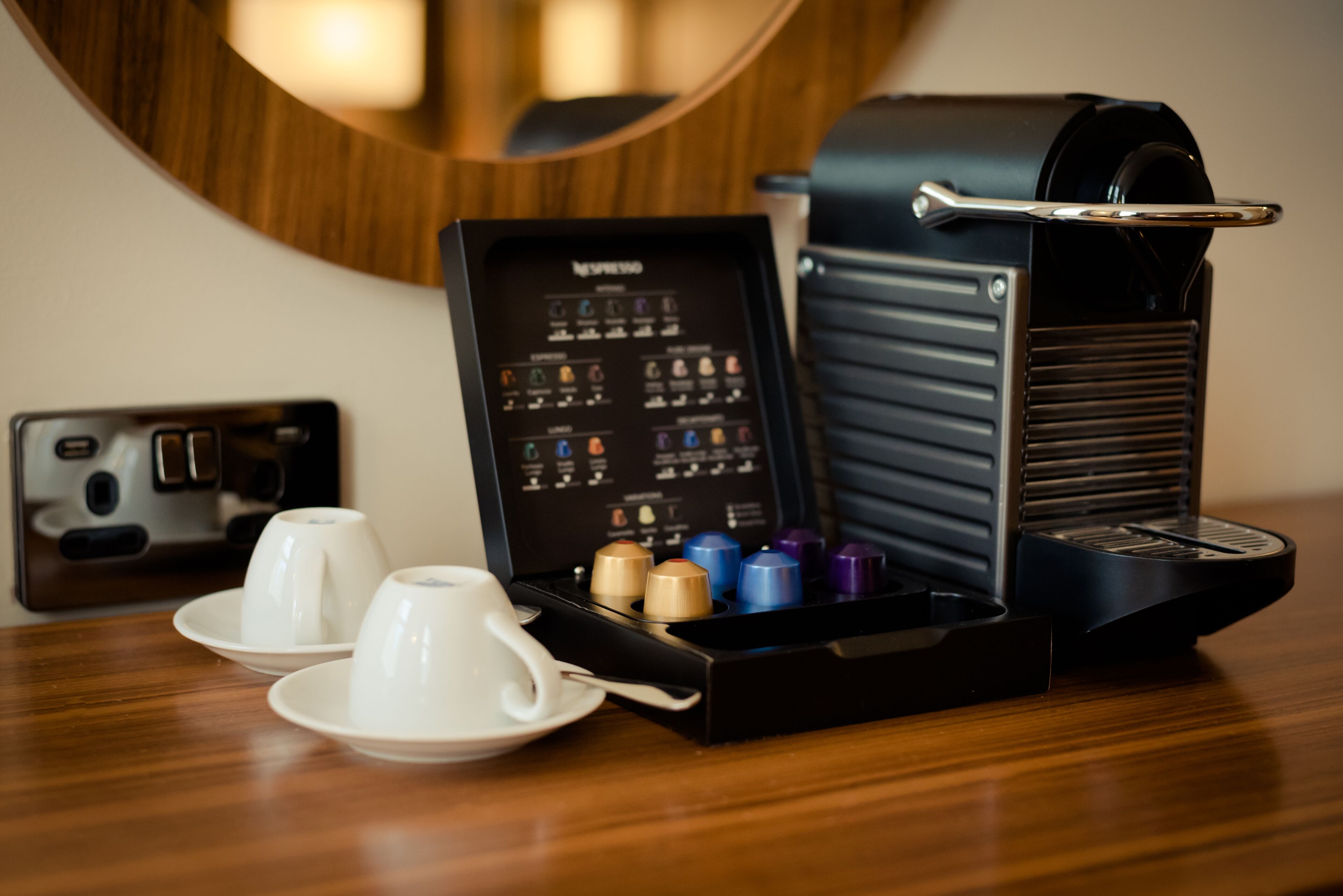 A coffee machine with a selection of coffee pods and two white cups on a wooden table.