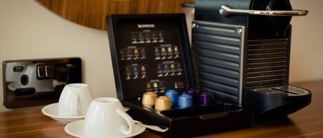 A coffee machine with a selection of coffee pods and two white cups on a wooden table.