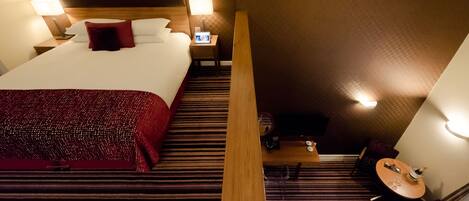 A hotel room with a large bed, two bedside tables with lamps, a small table with a chair, and a TV on a stand.