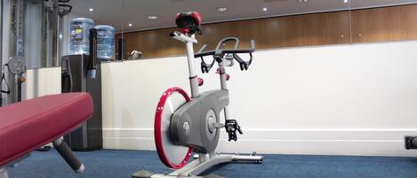 Un gimnasio con una bicicleta estática, un banco y dispensadores de agua.