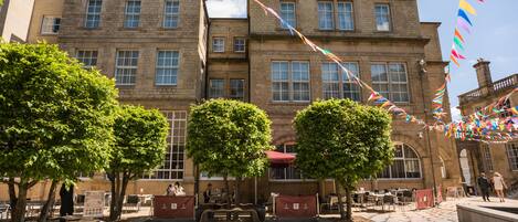 Un bâtiment historique doté d’une cour, d’un espace extérieur aménagé pour s’asseoir et d’un mât où flotte un drapeau.