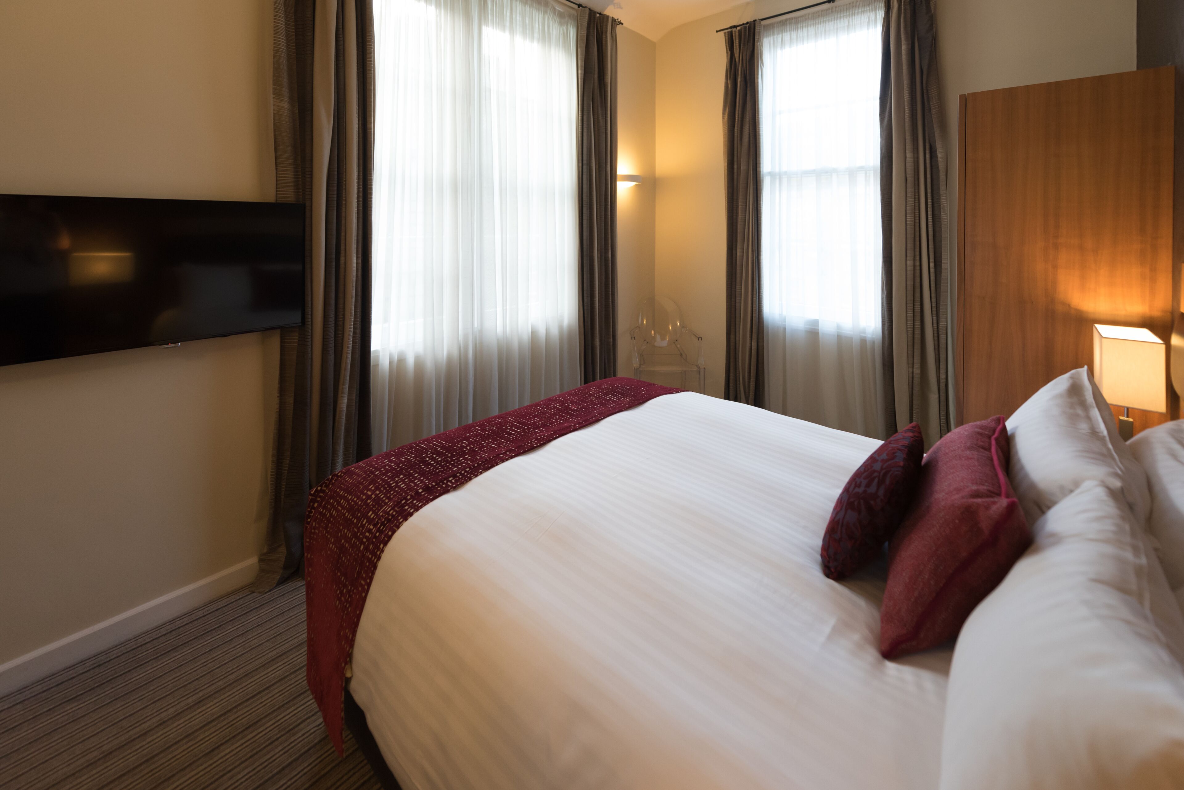 Une chambre d’hôtel avec un grand lit, un téléviseur à écran plat fixé au mur et une fenêtre avec des rideaux.