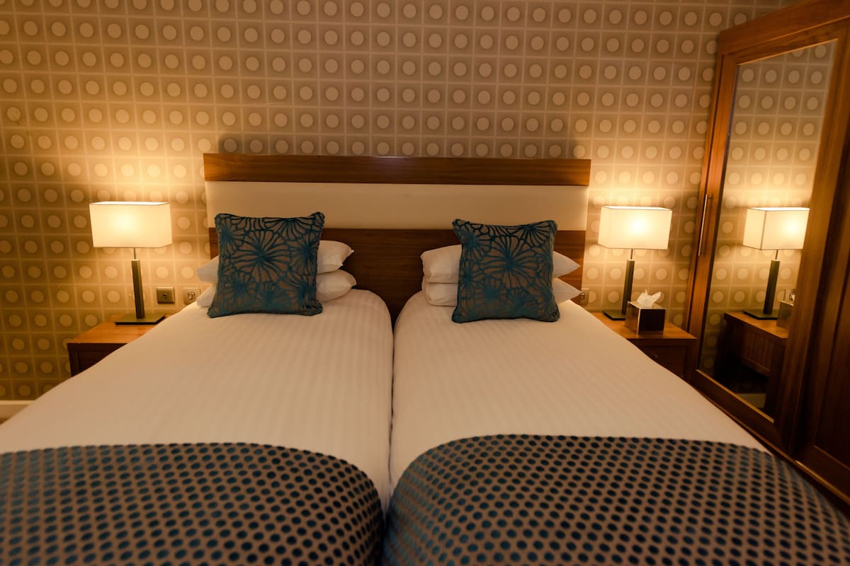 A double bed with a wooden headboard, two bedside tables with lamps, and patterned wall wallpaper.