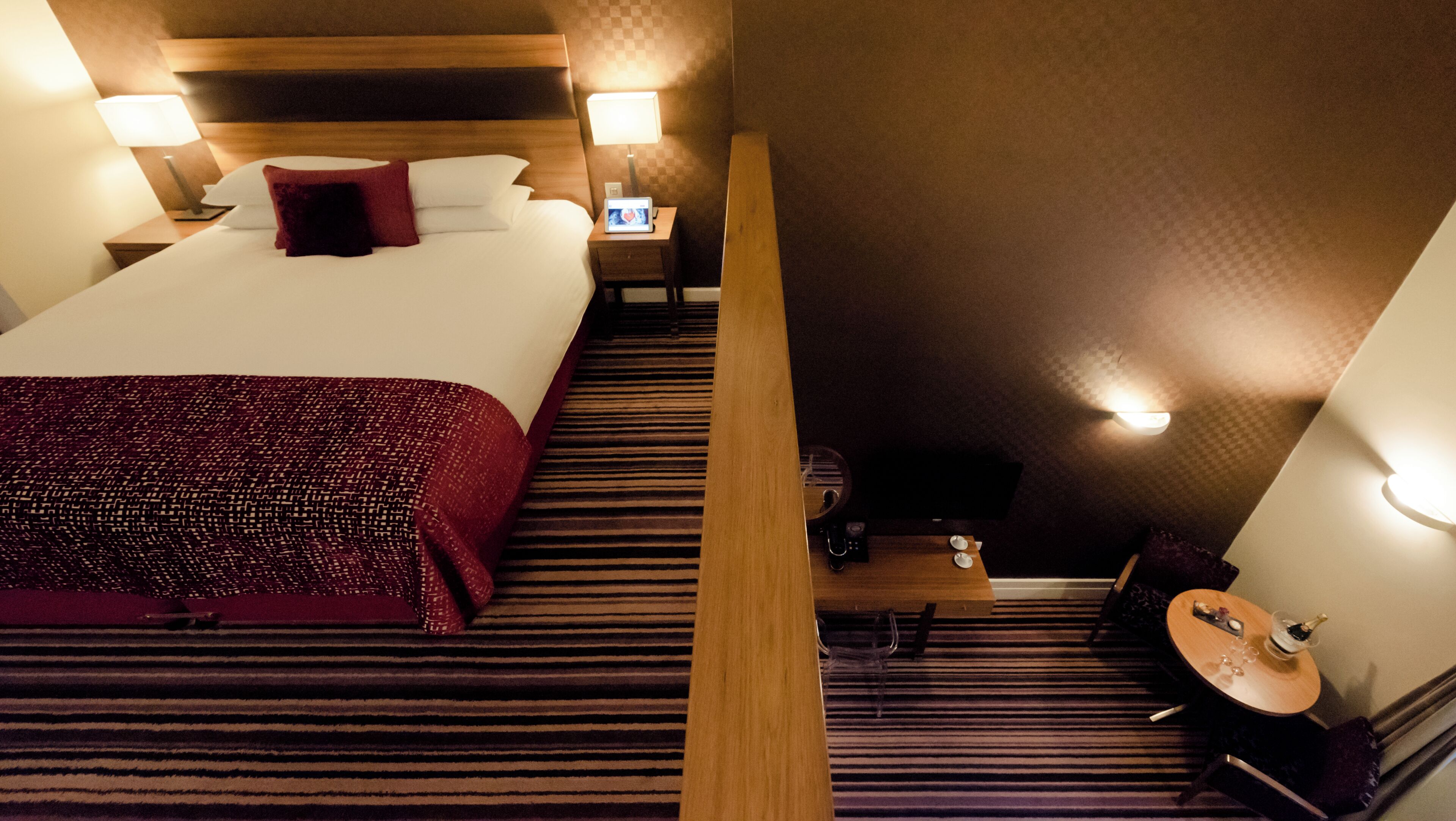 Een hotelkamer met een groot bed, twee nachtkastjes met lampen, een kleine tafel met een stoel en een tv op een dressoir.
