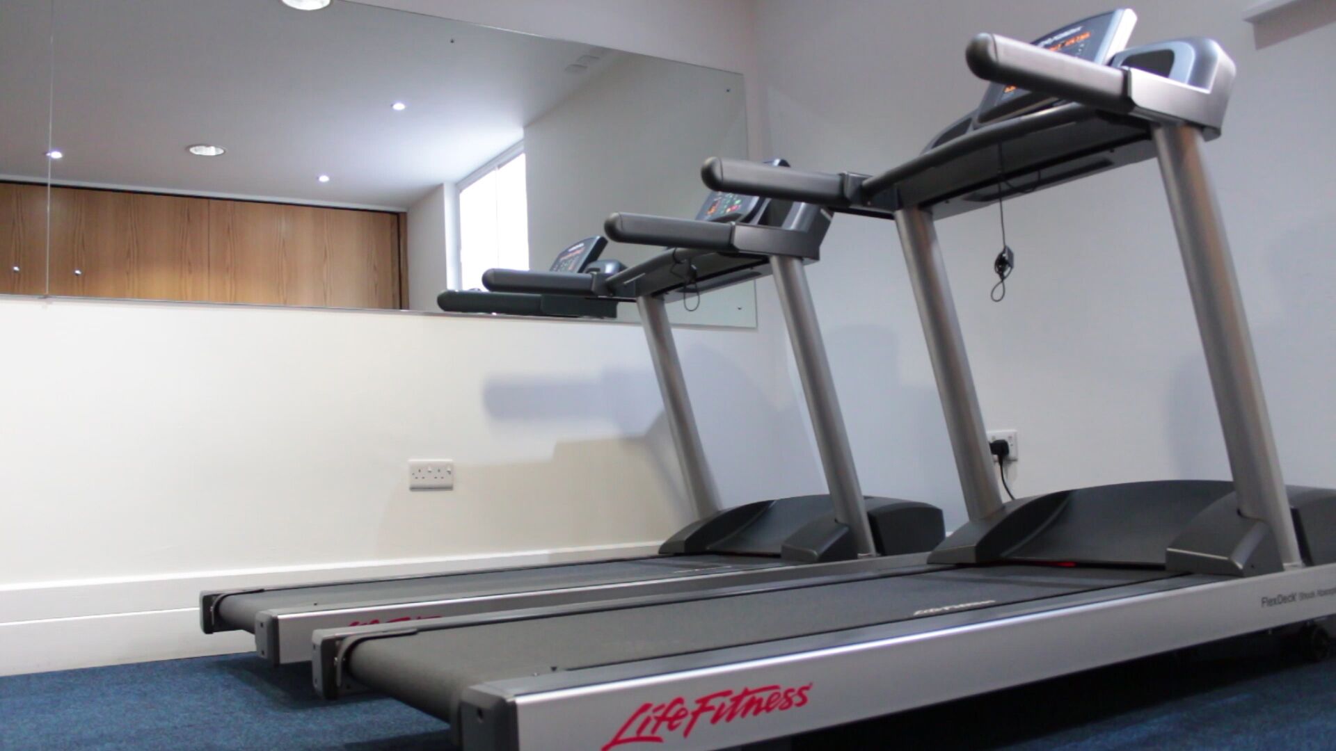 A treadmill in a room with a wooden cabinet and a mirror on the wall.