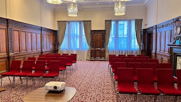 A conference room with red chairs arranged in rows, a projector on a table, and large windows with curtains.