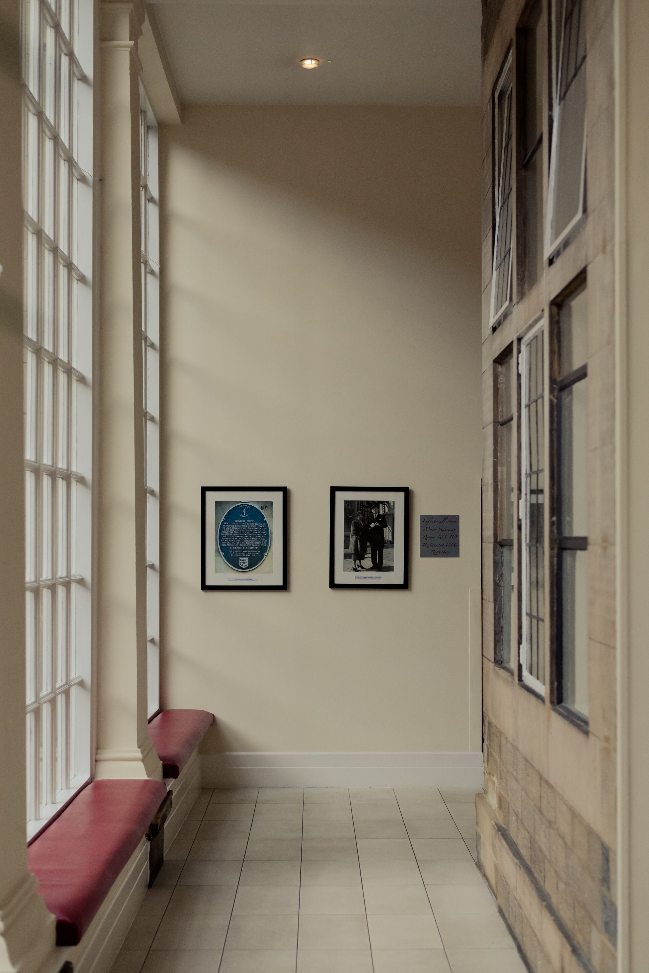 Un pasillo con un banco, una placa enmarcada y una fotografía en la pared.