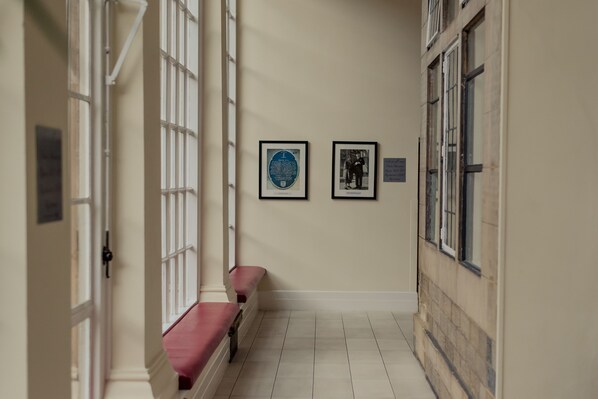 Um corredor com um banco, fotografias históricas emolduradas e uma porta.