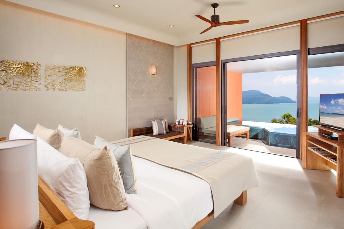 A modern bedroom with a large bed, a TV, and a balcony with a view of the sea.