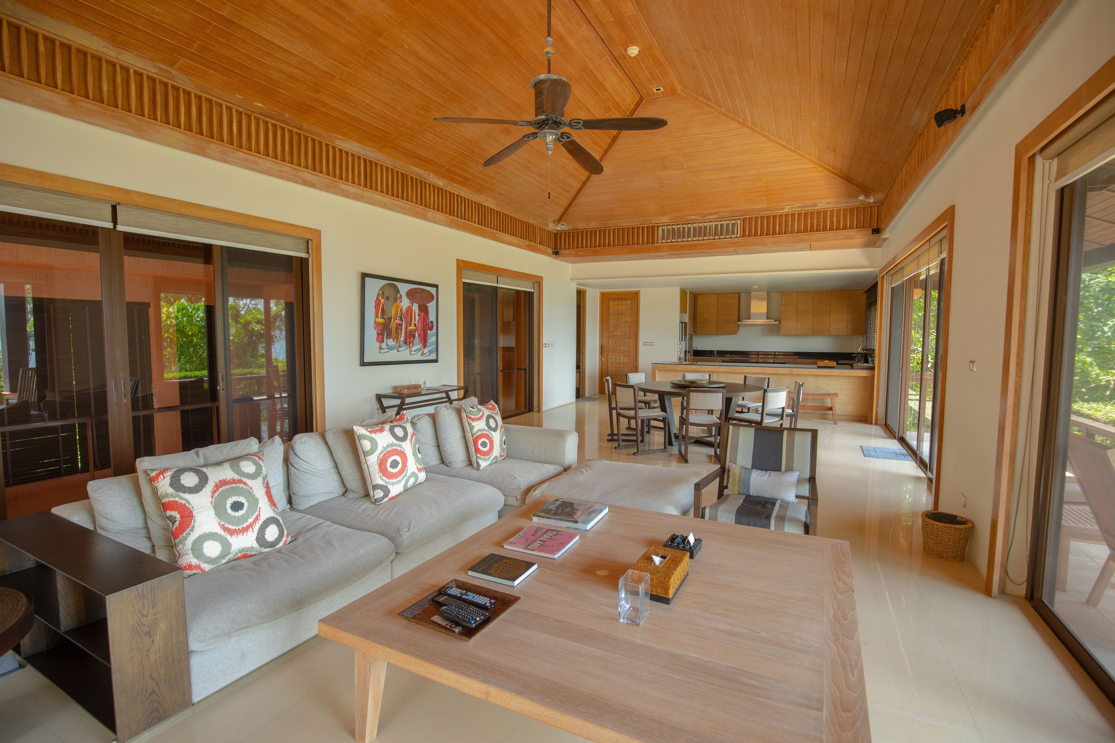 A modern living room with a wooden ceiling, a sofa set, a coffee table, and a kitchen in the background.
