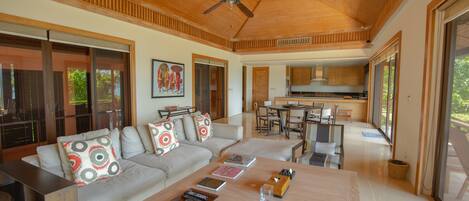 A modern living room with a wooden ceiling, a sofa set, a coffee table, and a kitchen in the background.