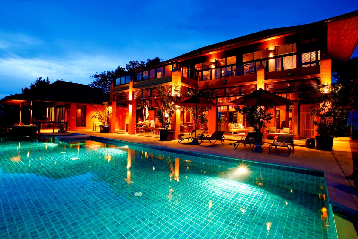 A modern hotel with a swimming pool, outdoor seating, and a well-lit facade.