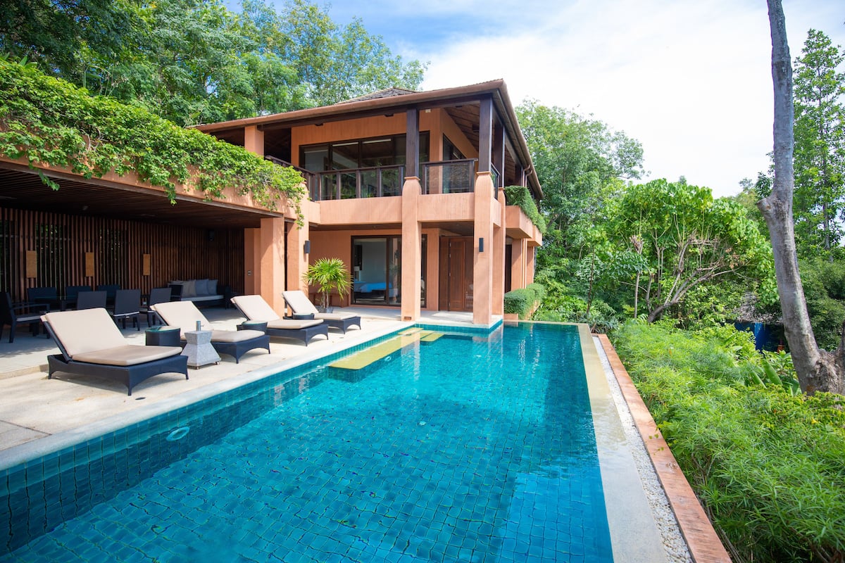 A modern house with a pool, lounge chairs, and a balcony overlooking the greenery.