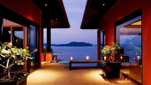 A modern building with large glass windows, a wooden deck, and a view of a body of water and mountains. - Sri Panwa Phuket Luxury Pool Villa Hotel (Wichit)