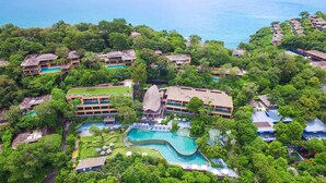 An aerial view of a resort with multiple buildings, a large central pool, and lush greenery. - Sri Panwa Phuket Luxury Pool Villa Hotel (Wichit)