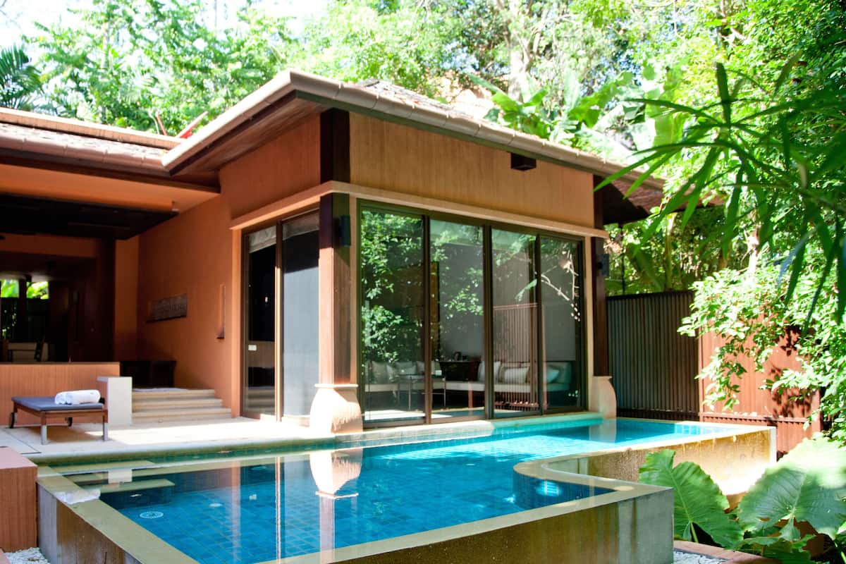 A modern house with a swimming pool, a covered patio, and a view of the surrounding greenery.