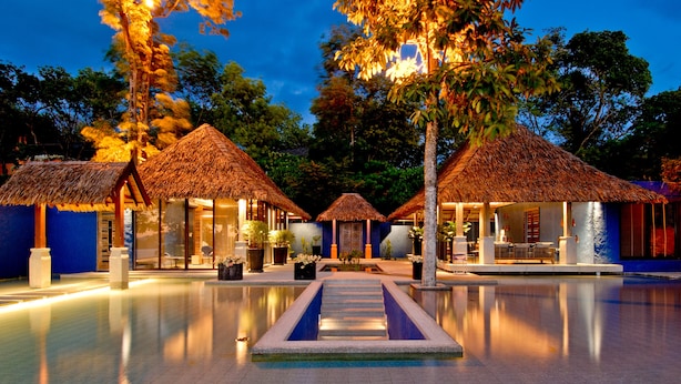 A pool area with thatched-roof structures, a clear pool, and a blue-tiled floor. - Sri Panwa Phuket Luxury Pool Villa Hotel (Wichit)