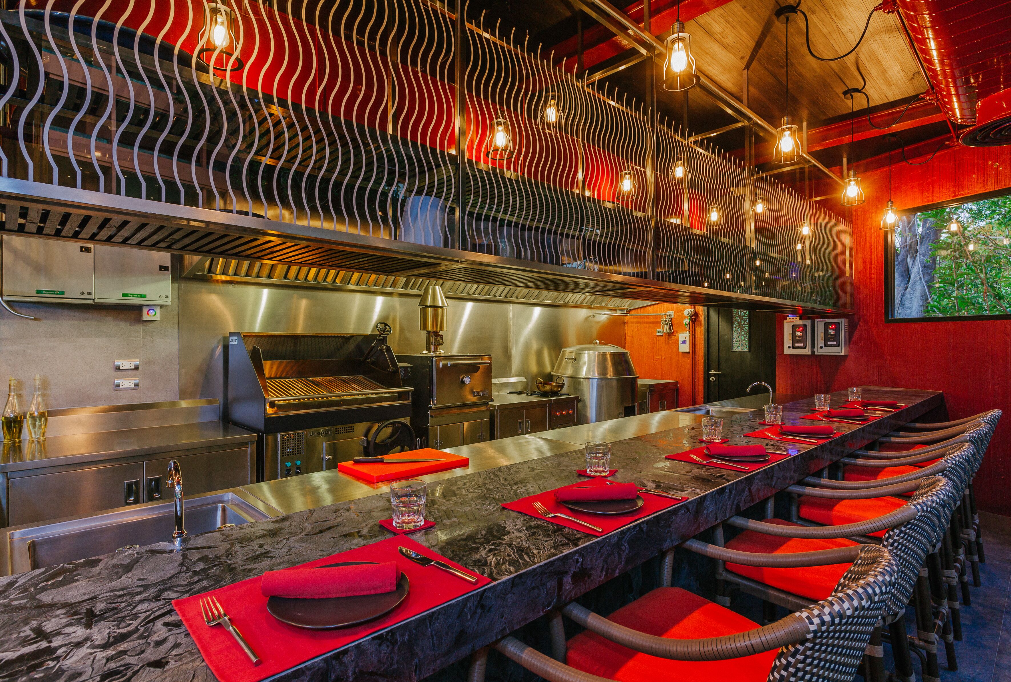 A restaurant with a long counter, red chairs, and a modern kitchen in the background.