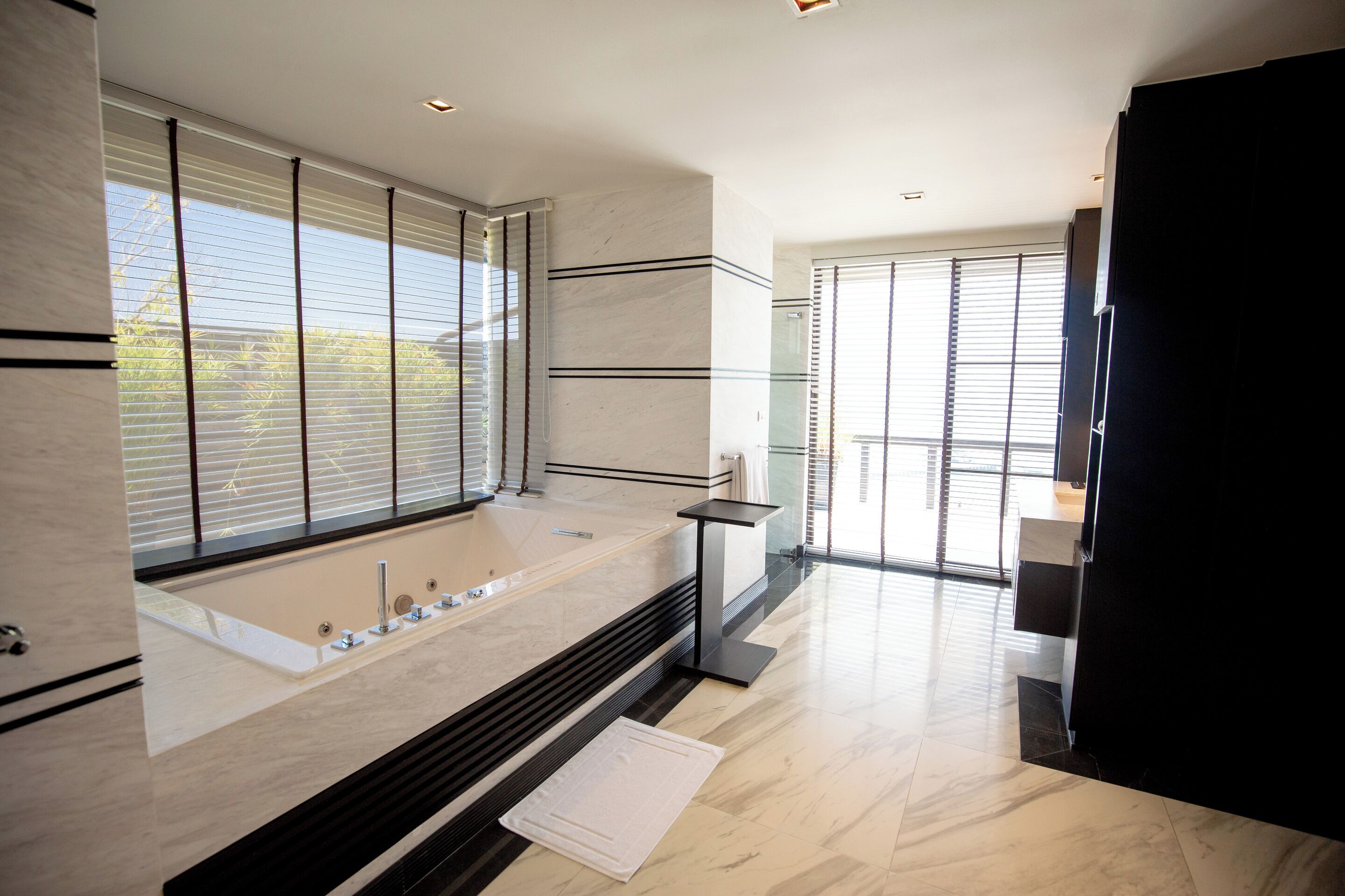 A modern bathroom with a large bathtub, a vanity, and a window with blinds.