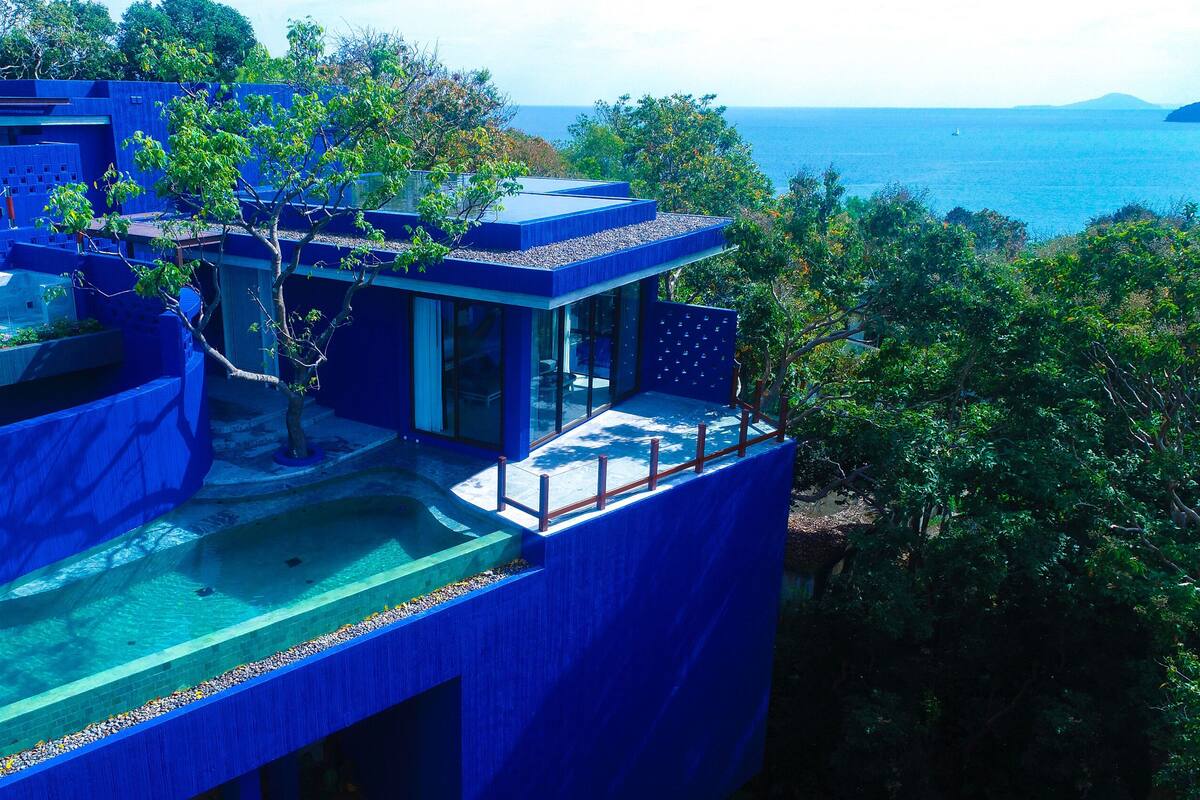 A modern architectural structure with a pool, surrounded by lush greenery and overlooking a body of water.