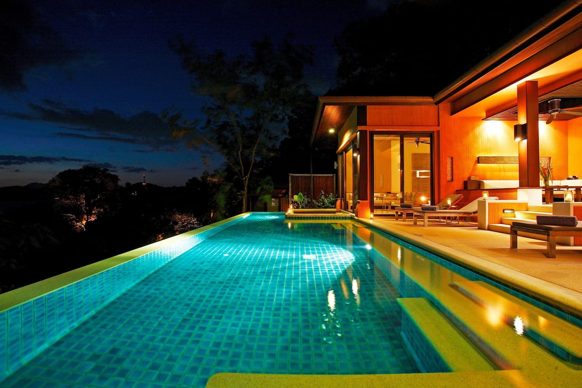 A swimming pool with a tiled edge, a wooden deck, and a lounge area with seating and a table.