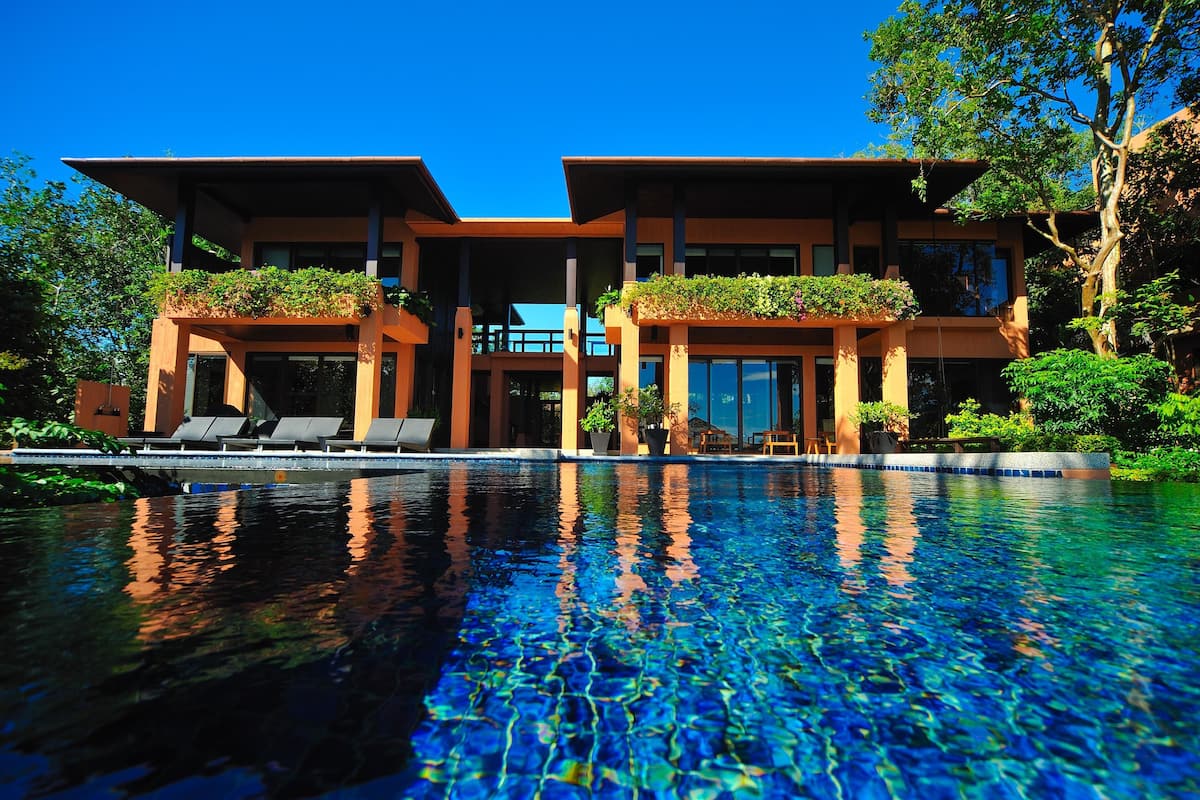 A modern hotel with a pool, outdoor seating, and lush greenery.