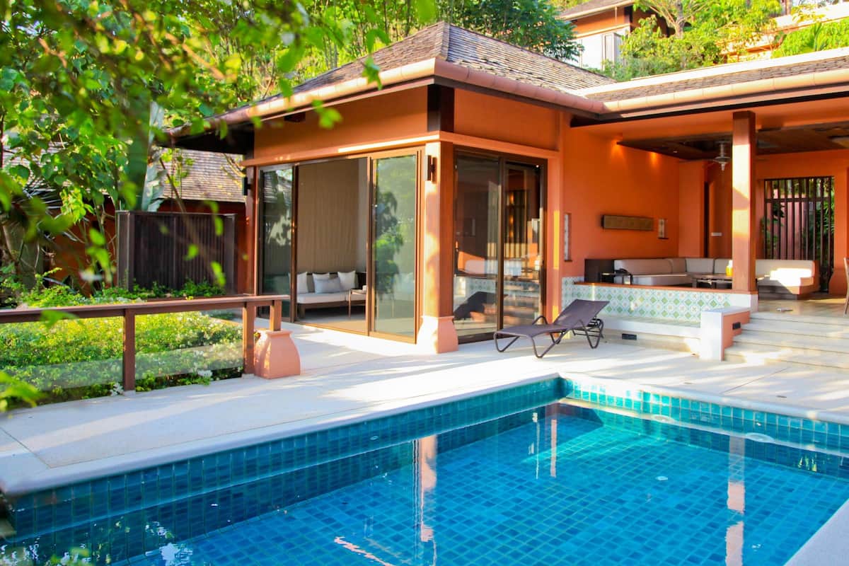 A modern outdoor pool area with a glass-enclosed lounge, seating, and a clear blue pool.