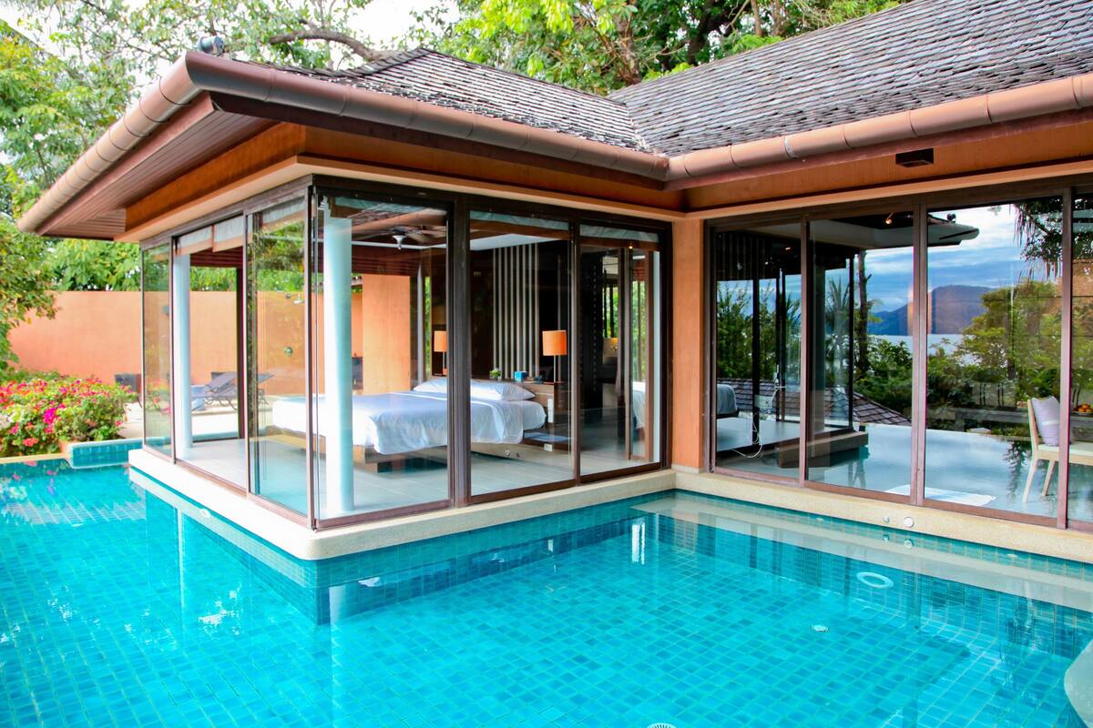 A modern hotel with a glass-enclosed pool area, a bedroom with a bed and a nightstand, and a view of the surrounding landscape.