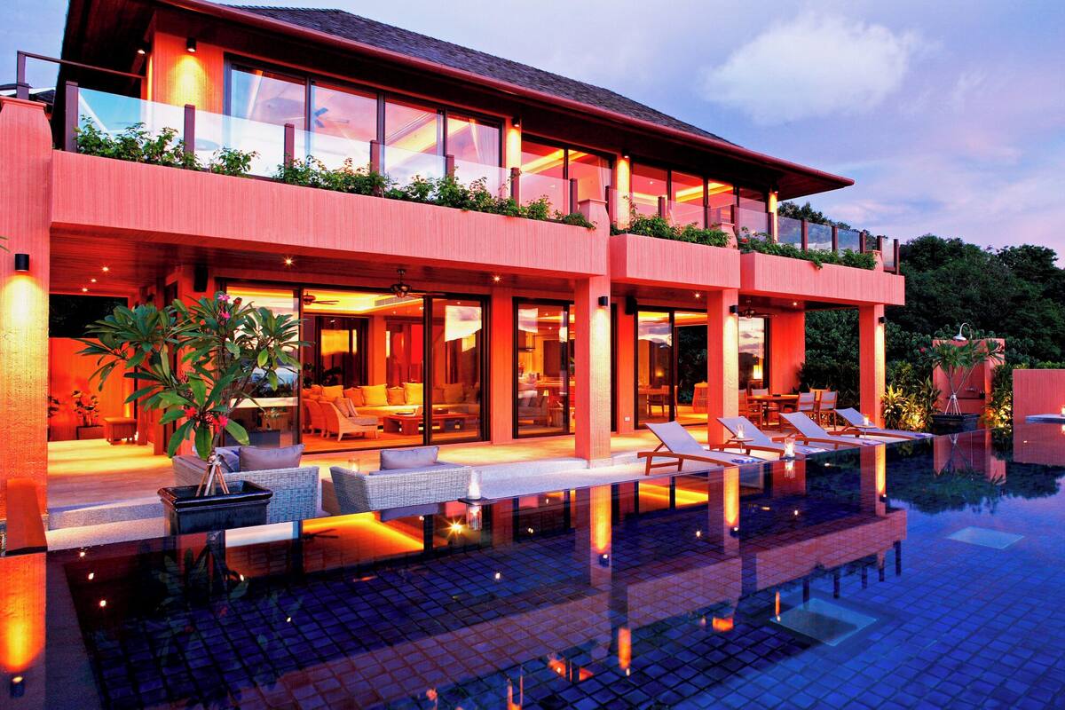 A modern two-story house with a large glass balcony, a swimming pool, and outdoor seating.