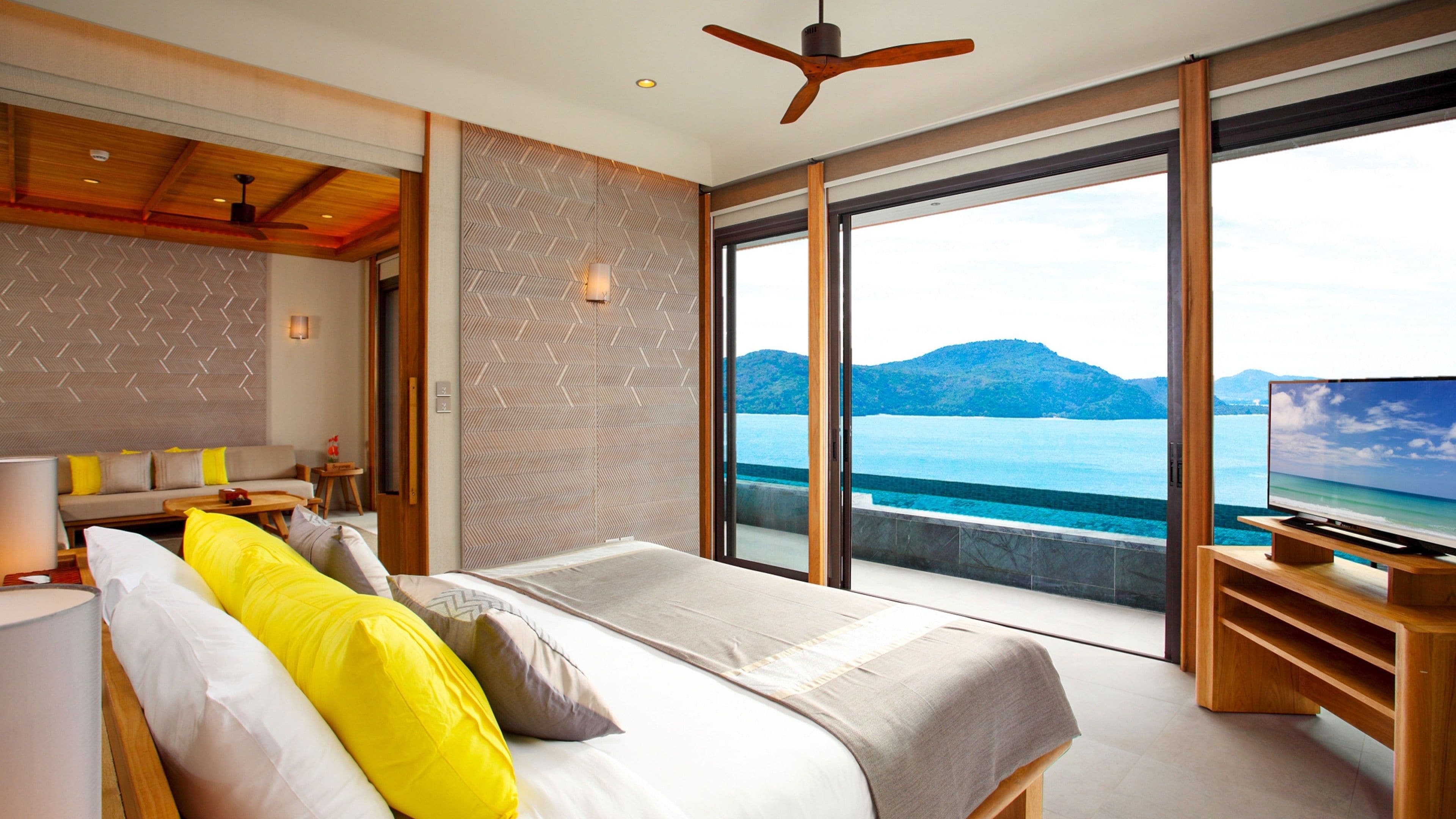 A modern hotel room with a large bed, a TV, and a balcony with a sea view.