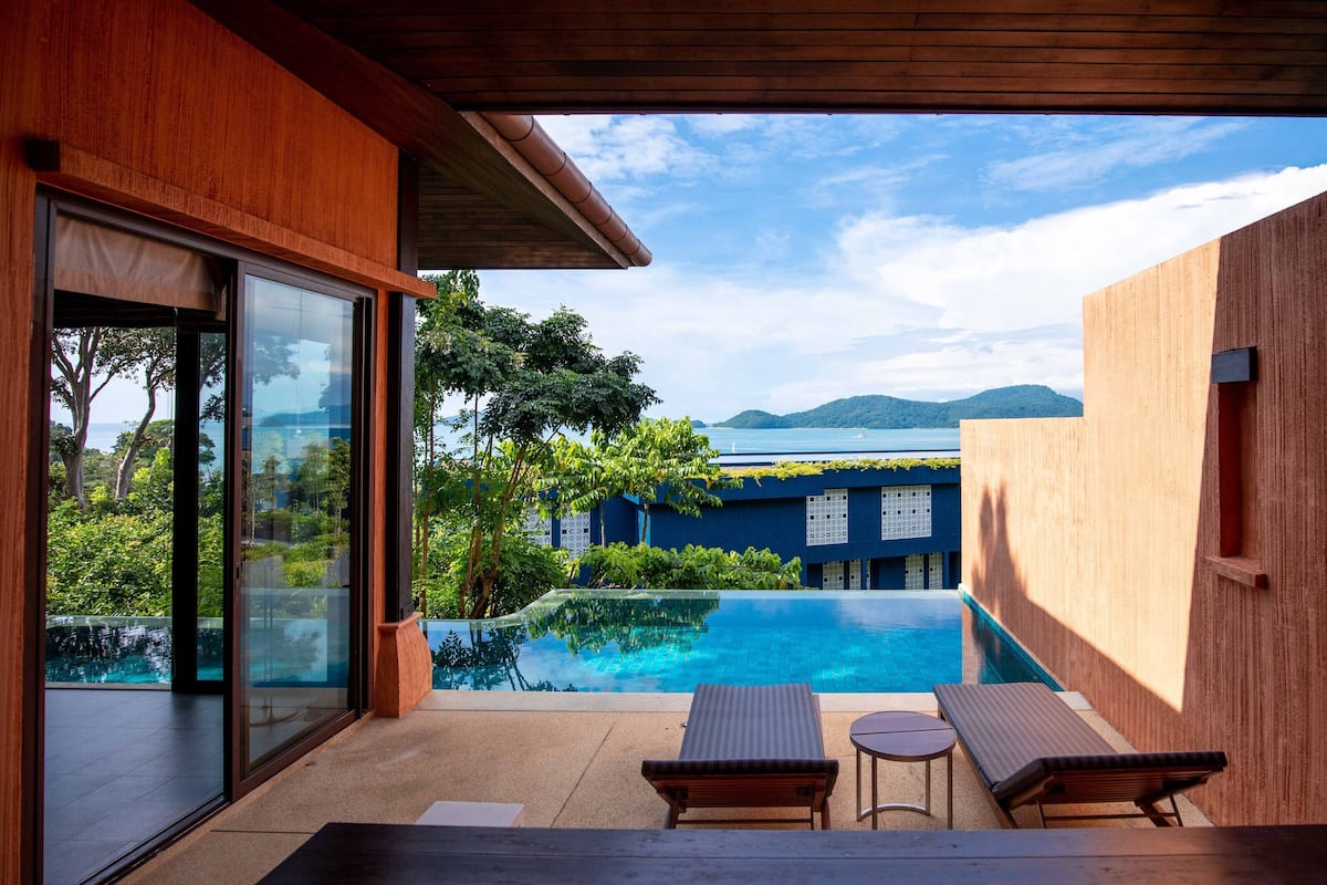A modern outdoor pool area with two lounge chairs and a small table, overlooking a clear blue pool and a distant view of a mountainous landscape.