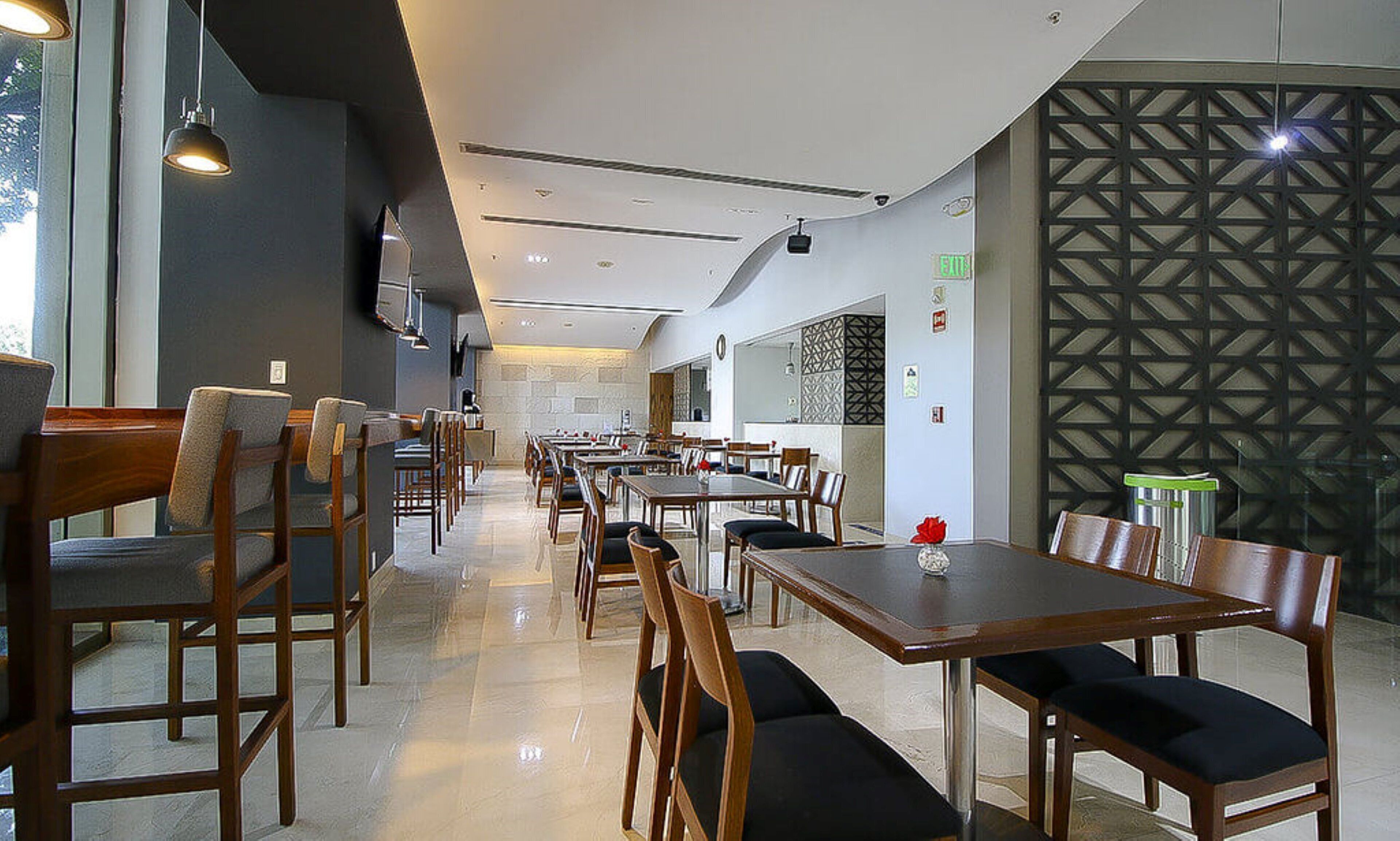 A spacious restaurant with multiple tables and chairs, a modern ceiling design, and a decorative wall pattern.
