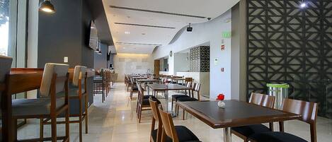 A spacious restaurant with multiple tables and chairs, a modern ceiling design, and a decorative wall pattern.