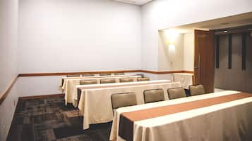 Un salón de conferencias con varias mesas y sillas, suelo alfombrado y una puerta de madera.