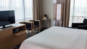 A hotel room with a large bed, a TV on a wooden dresser, two chairs, a small table with a coffee maker, and a lamp.