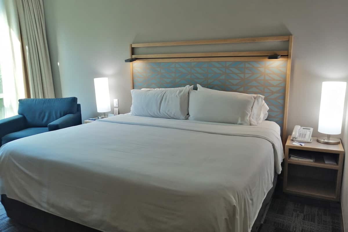 A hotel room with a large bed, a blue armchair, bedside tables with lamps, and a patterned wall.