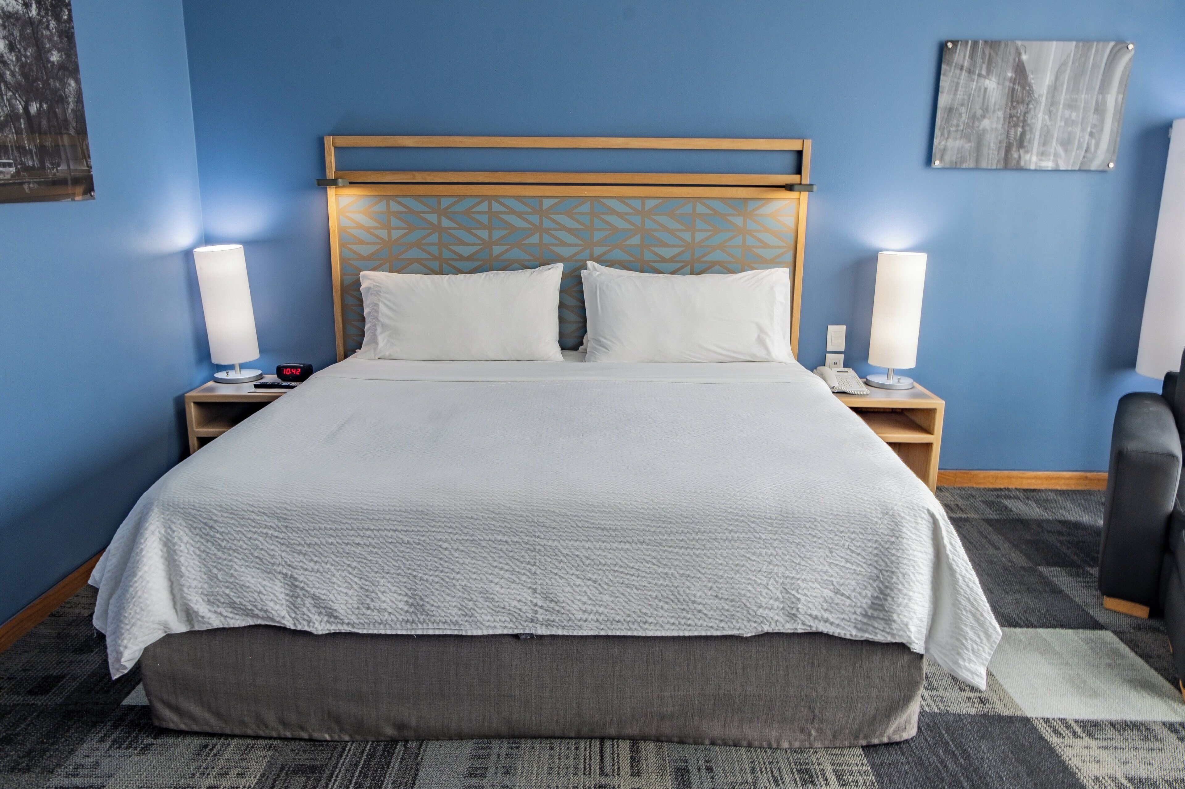 Una habitación de hotel con una cama grande, dos mesitas de noche, un cabecero con diseño geométrico y una obra de arte colgada en la pared.