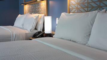 A hotel room with two beds, each with white linens and pillows, a bedside table with a lamp, and a phone.