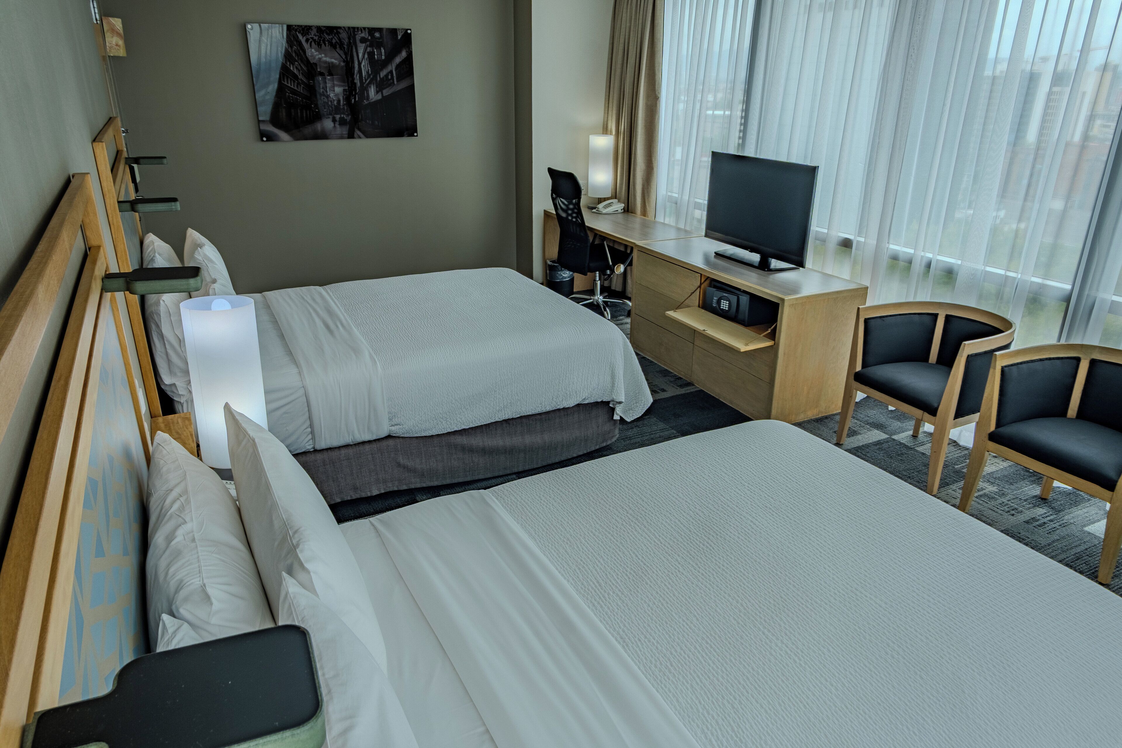 Une chambre d’hôtel avec deux lits, un bureau avec une télévision, une chaise et une fenêtre avec des rideaux.