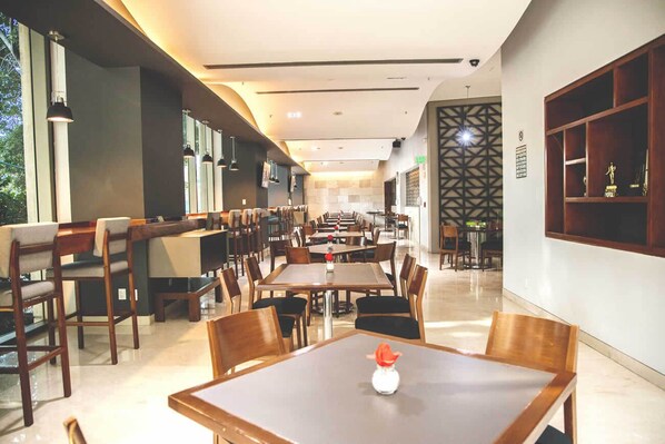 A spacious restaurant with multiple tables and chairs, a long counter, and a decorative wall with a geometric pattern.