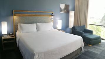 Habitación de hotel con una cama grande, lámparas de noche, una silla y ventana con vistas.