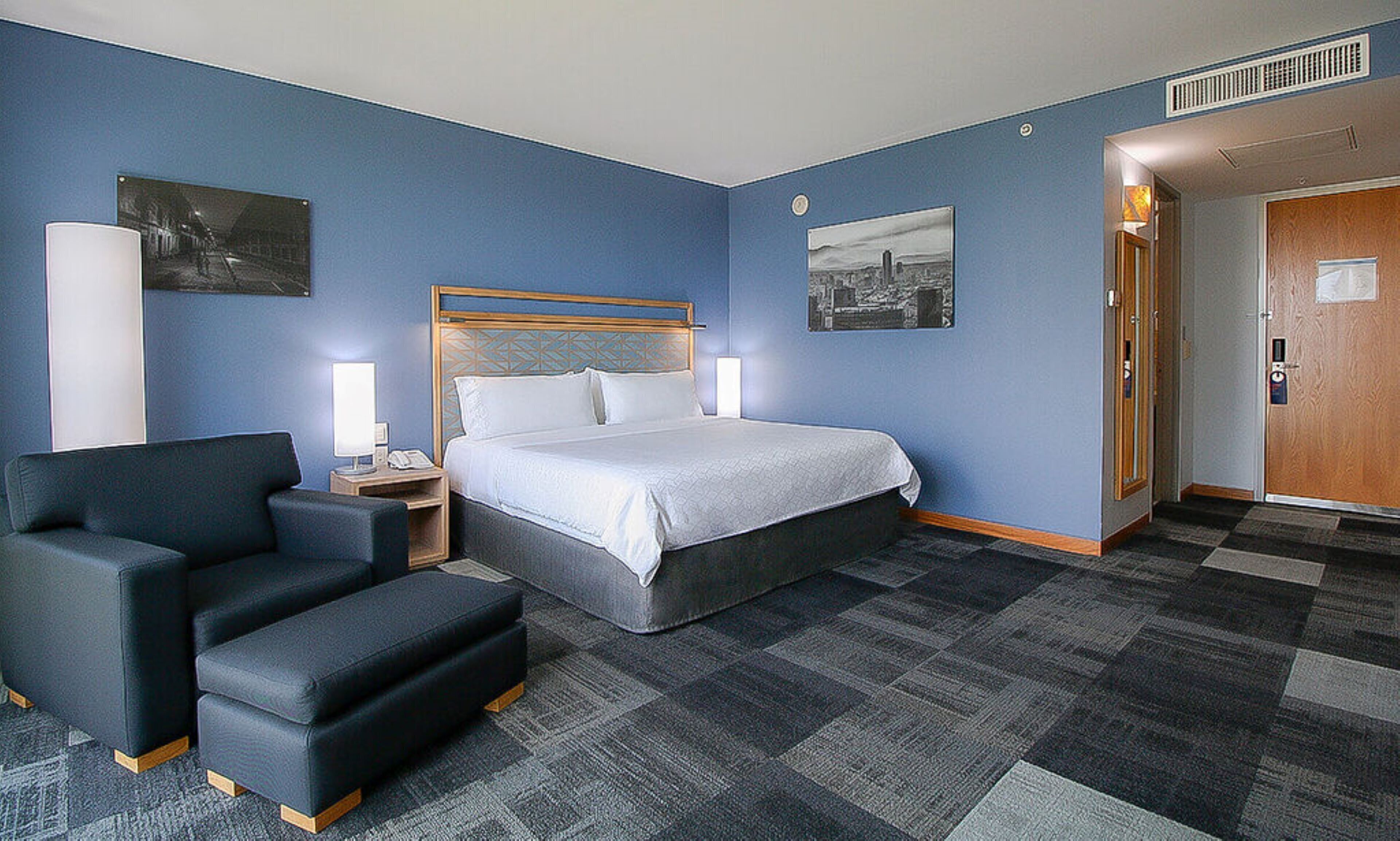 A hotel room with a bed, a desk, a chair, and a door.