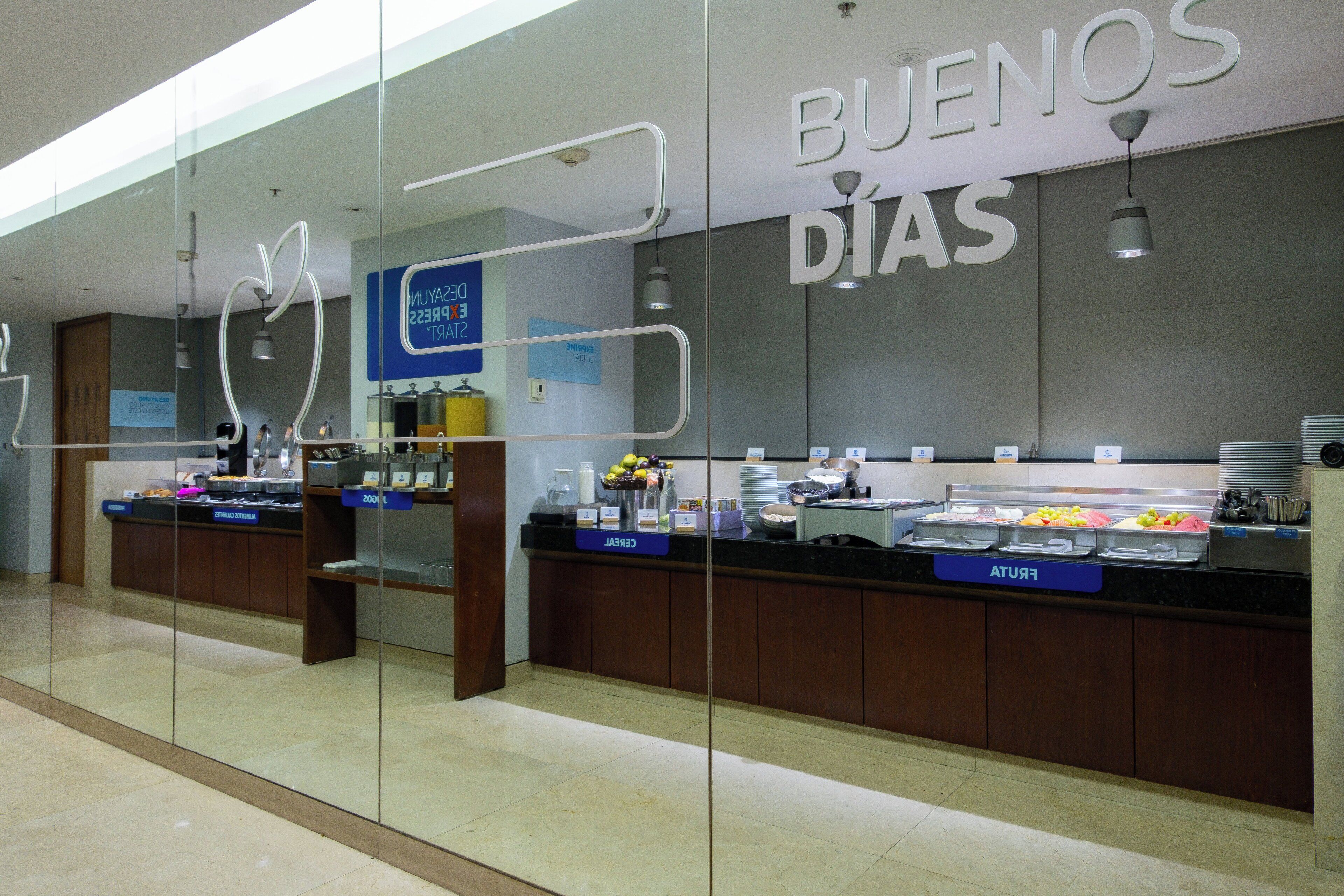 A breakfast area with a counter displaying various food items and a sign that reads "BUENOS DÍAS".