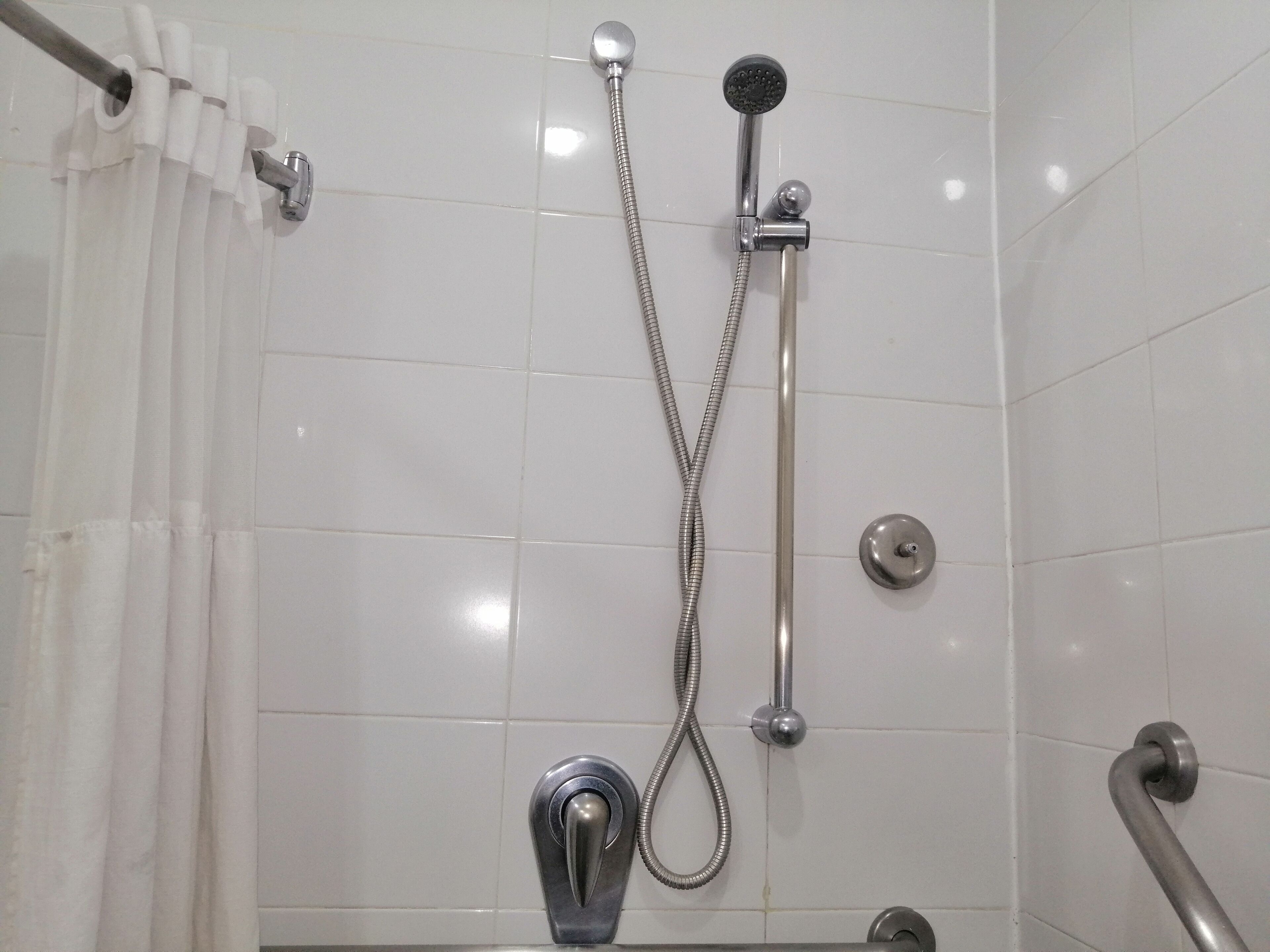A shower with a handheld showerhead and a fixed showerhead, both mounted on a wall with white tiles.