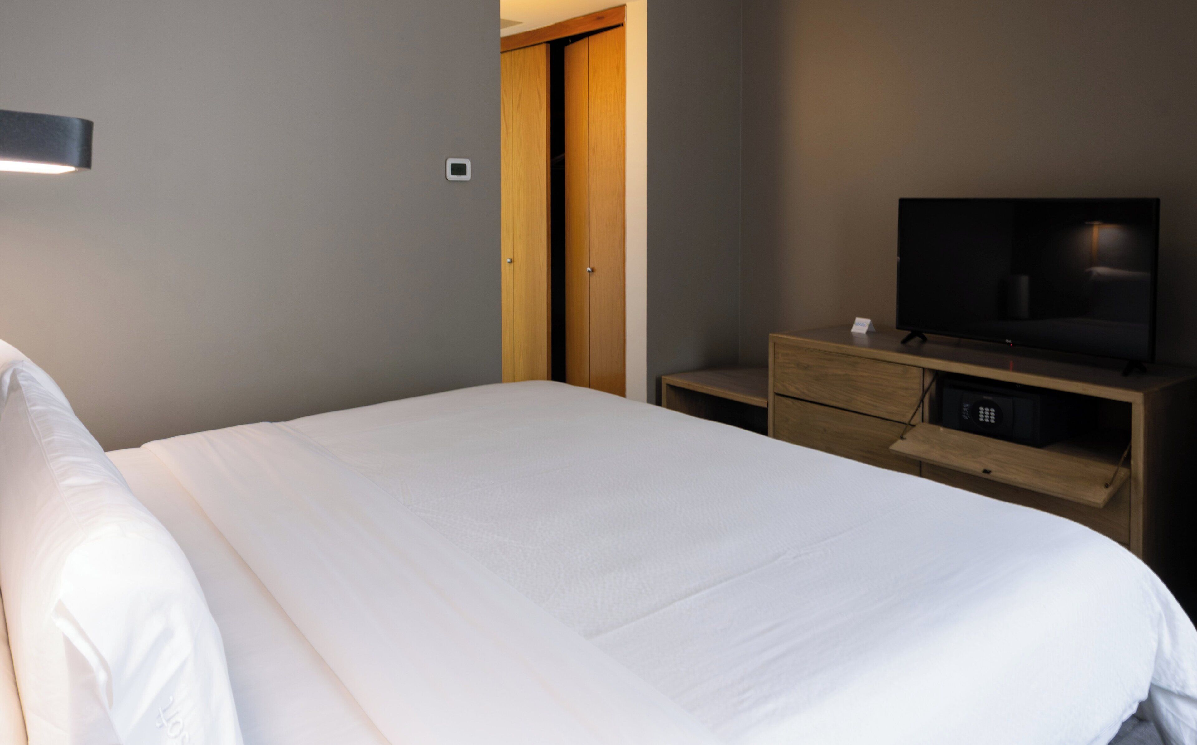 A neatly made bed in a hotel room with a television on a wooden stand and a small drawer below it.