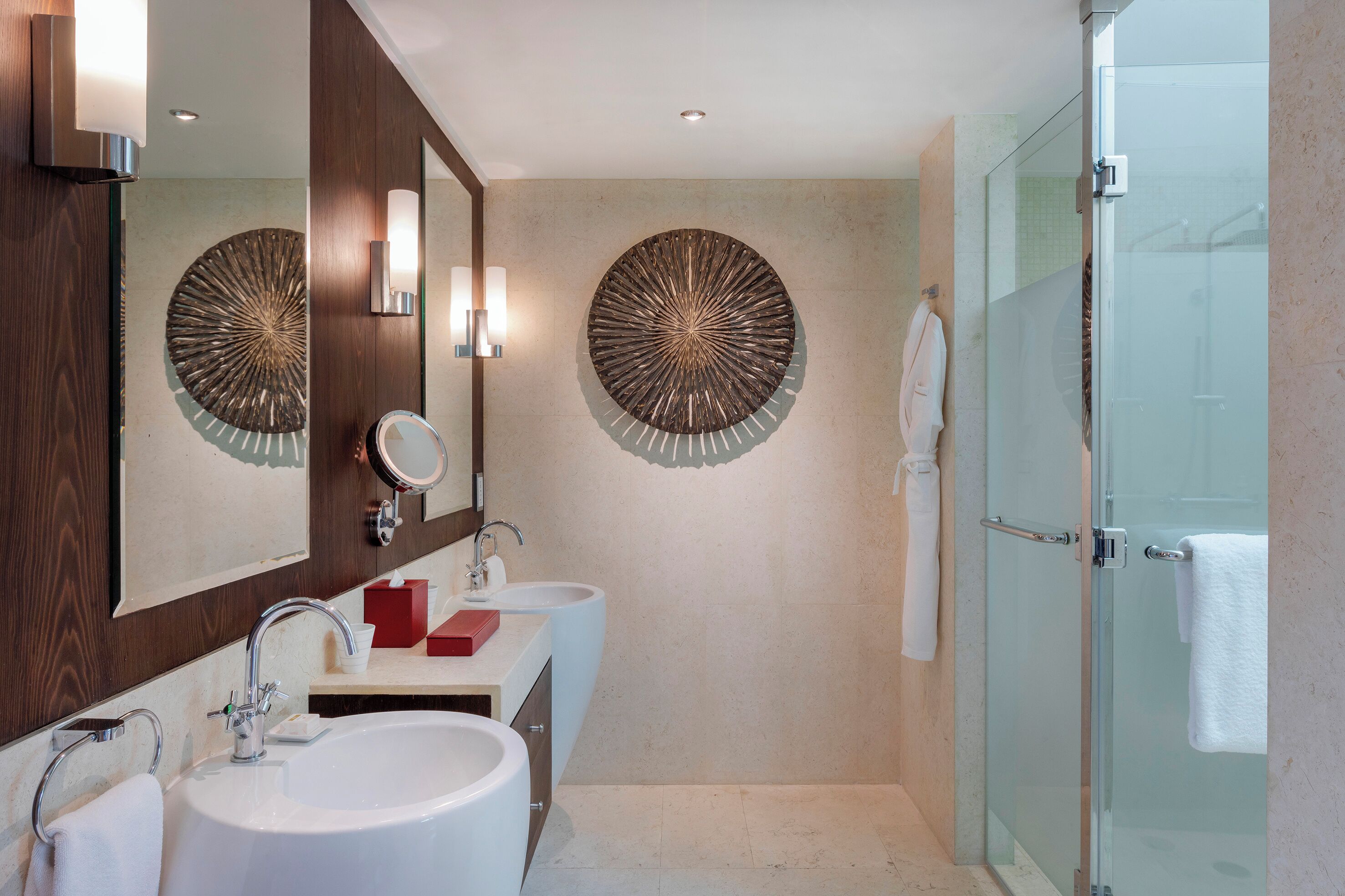 A modern bathroom with two sinks, a large mirror, wall sconces, and a glass shower enclosure.