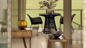 A balcony with a view of a golf course, a table with chairs, and a vase with plants.